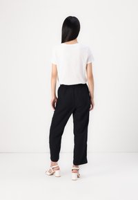 Camicia bianca a maniche corte abbinata a pantaloni neri larghi e sandali bianchi con tacco a blocco. Tessuto liscio e vestibilità rilassata. Design semplice.