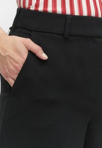 Svarta skräddarsydda byxor med en slät yta, som har en sidoficka och en platt midjeresår. Materialet verkar vara lätt och andningsaktivt.