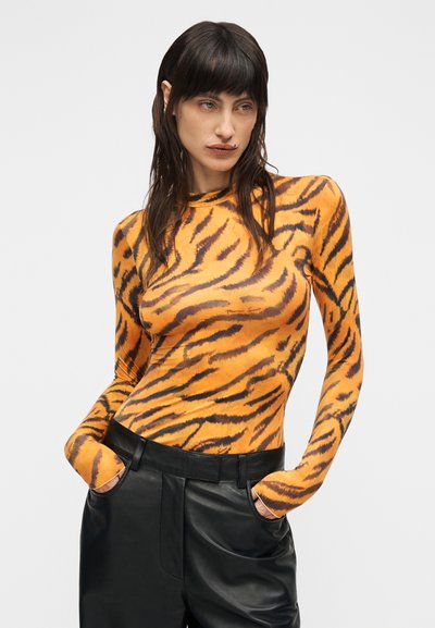 Πλεχτό τοπ με μακριά μανίκια σε πορτοκαλί χρώμα με μαύρες ρίγες τίγρης, με ψηλό λαιμόκοψη. Συνδυάζεται με μαύρο δερμάτινο παντελόνι ψηλόμεσο.