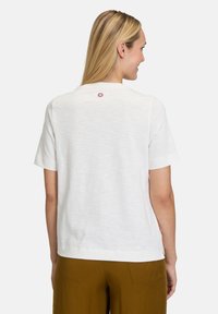 Weißes T-Shirt mit kurzen Ärmeln und lockerer Passform, mit einem dezenten gestickten Design nahe dem Ausschnitt. Weicher, strukturierter Stoff.