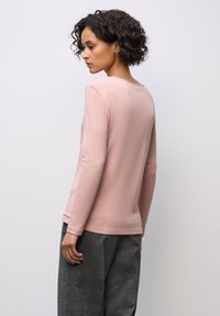 Hellrosa Langarmshirt aus weichem Stoff mit rundem Halsausschnitt und engem Schnitt. Kombiniert mit grau karierten Hosen.