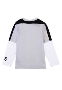 Maglietta a maniche lunghe con corpo grigio, spalle nere e maniche bianche. Presenta un numero "6" stampato sulla manica sinistra. Materiale in cotone.