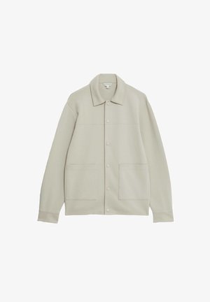 Chaqueta botón en color beige claro hecha de un tejido suave, con cuello, dos bolsillos frontales y un diseño simple y limpio.