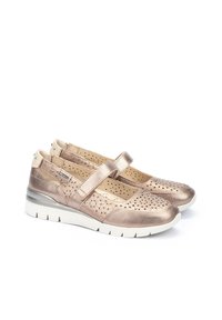 Chaussures en rose doré métallique avec un design perforé, bout rond, sangle réglable et semelle blanche contrastante. Texture lisse et légères.