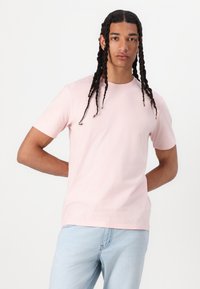 Svetlo roza bombažna majica s kratkimi rokavi, okroglo izrezom in sproščenim krojem, v kombinaciji s svetlo modrimi džinsom.