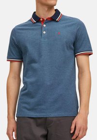 Koszulka polo z krótkim rękawem w heatherskiej niebieskiej bawełnie, z czerwonym kołnierzykiem i paskami w kolorze granatowym i białym. Detal z podwójnym zapięciem na guziki.