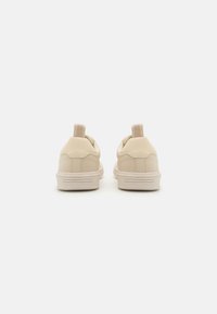 Beige faux leather sneakers with textured panels, rounded shape, and pull tabs at the back. Features a white rubber sole with grooves.