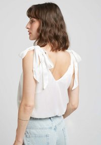Haut sans manches blanc avec des bretelles à nouer, design V au dos, tissu texturé et coupe décontractée, associé à un short en denim bleu clair.