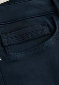 Tessuto di denim blu scuro con cuciture dettagliate intorno a una piccola tasca frontale di un paio di jeans.