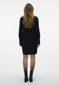 Abito nero in maglia con silhouette aderente, maniche lunghe e motivo testurizzato. Indossato con stivali neri sopra il ginocchio e calze grigie.