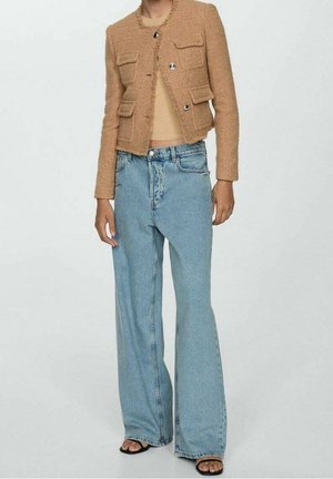 Persoon draagt een bruine cropped gestructureerde jas, een beige geribde top, lichtblauwe wijde jeans met hoge taille en zwarte sandalen met open tenen.