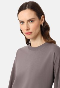 Sweatshirt gris avec un col rond, un col côtelé et une coupe ample. Texture lisse, manches longues et design minimaliste.