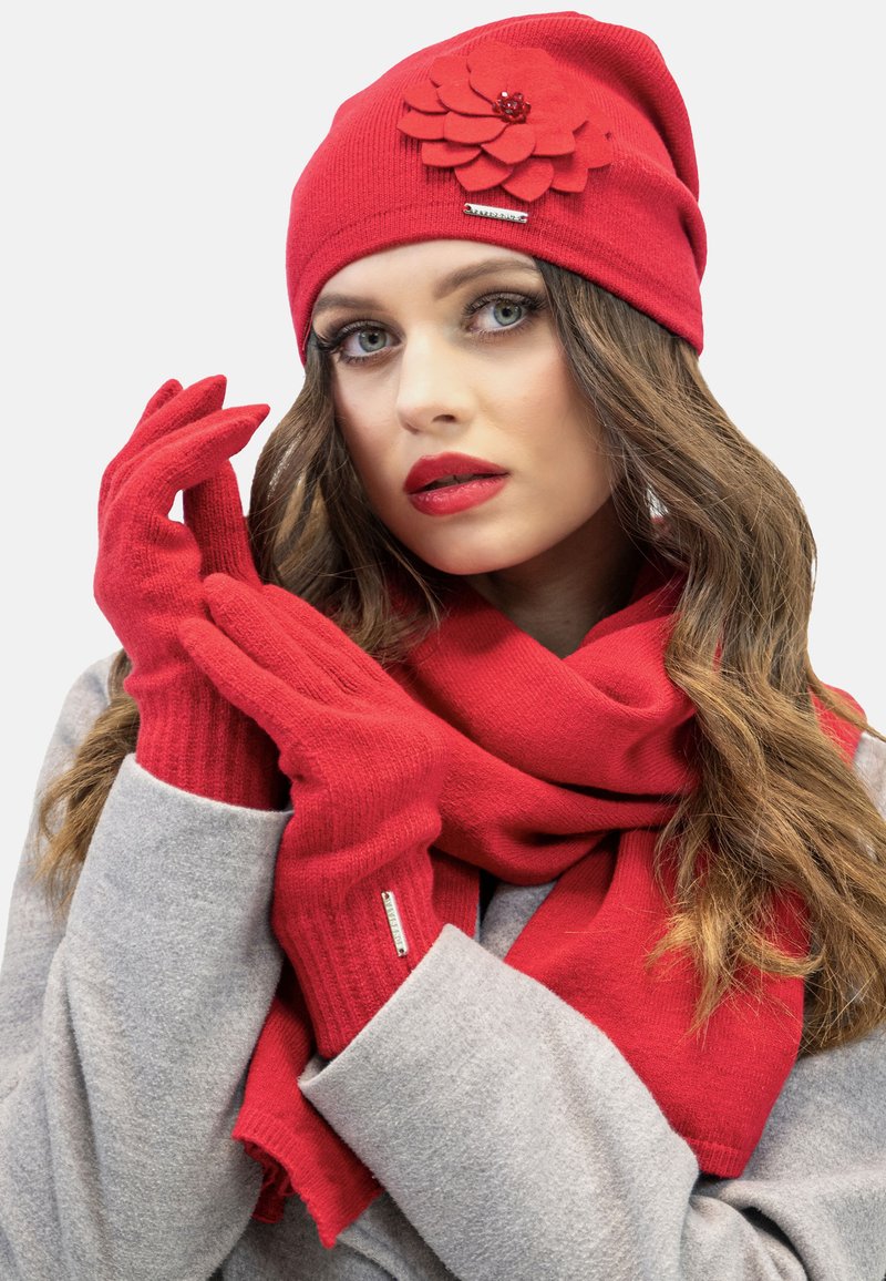 Czerwona dziana czapka beanie z detalem w postaci filcowego kwiatu, pasujące czerwone rękawiczki i szalik. Miękka tekstura i elegancki design; wszystko w jaskrawoczerwonym kolorze.