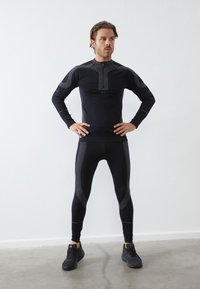 Svart träningstopp och leggings med ribbade detaljer. Tätt sittande design, hög hals med dragkedja, lång ärm, och texturerade mönster.
