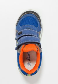 Zapatilla infantil azul y naranja con tiras de velcro, fabricada en tejido de malla, y con la talla 25 marcada en el interior del zapato.
