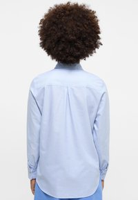 Camicia a maniche lunghe blu chiaro in cotone con colletto button-down e piega sul retro. Presenta polsini con bottone e orlo curvo.