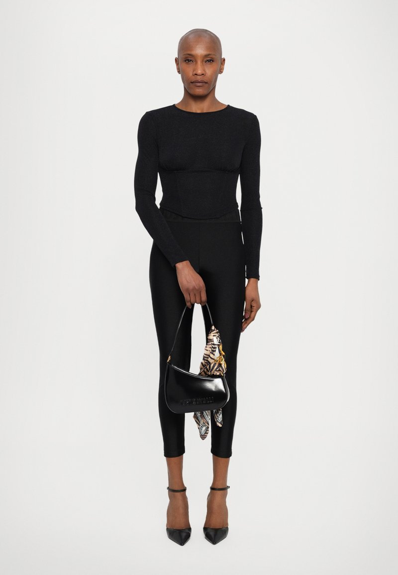 Μαύρο μπλουζάκι με μακριά μανίκια και εφαρμοστή σιλουέτα, συνδυασμένο με μαύρες κολάν και μια μικρή μαύρη τσάντα χεριού με σχέδιο.