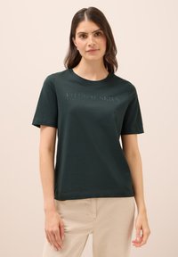 Camiseta de algodón verde oscuro con cuello redondo y mangas cortas. El texto "CIELOS ETERNOS" está grabado en un color a juego en el pecho.