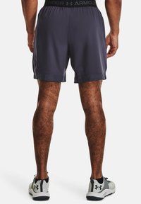 Pánské sportovní šortky, tmavě šedé, elastický pas s logem, lehká tkanina a volný střih. Nosené se šedými a černými teniskami.