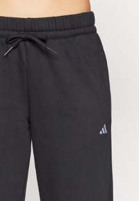 Black sweatpants made of soft fabric, featuring an elastic waistband with a drawstring and a small logo on the bottom left side.
