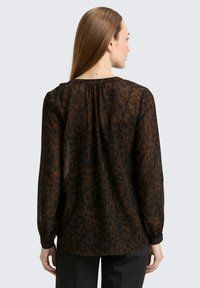 Braune durchsichtige Bluse mit einem Leopardenmuster, langen Ärmeln und einem gerafften Ausschnitt auf der Rückseite. Verfügt über eine lockere Passform und eine leichte Textur.