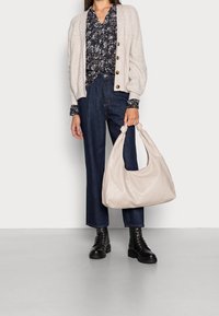 Beige nahkainen käsilaukku pyöreällä muodolla ja solmusomisteilla, yhdistettynä kukalliseen puseroon, harmaaseen neuletakkiin ja sinisiin leveälahkeisiin farkkuihin. Mustat nauhalliset saappaat.