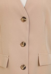 Gilet rosa chiaro con quattro grandi bottoni marmorizzati, texture liscia e due tasche laterali. Design semplice con vestibilità sagomata.