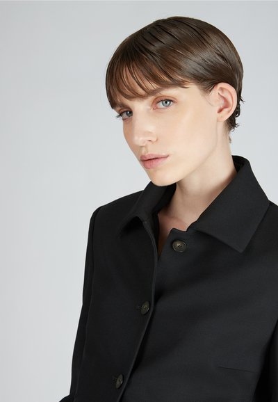 Giacca nera con bottoni, caratterizzata da un colletto rigido, tre bottoni e un tessuto liscio e sartoriale. Design semplice e silhouette strutturata.