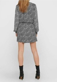 Vestido de lunares en blanco y negro con mangas largas, cintura entallada y falda acampanada, combinado con botas de tacón negro hasta la rodilla.