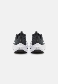 Scarpe atletiche in bianco e nero con tomaia texturizzata, colletto imbottito e suola ammortizzata. Presentano un logo Nike sul lato.
