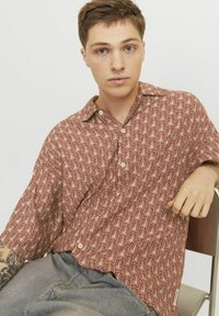 Camisa de manga corta y botones en color óxido con un patrón floral blanco; hecha de una tela ligera, presenta un collar extendido y un corte relajado.