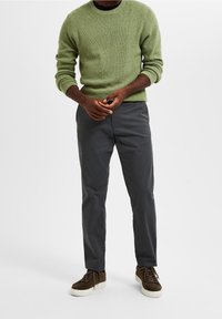 Groene getextureerde gebreide trui, donkergrijze broek en bruine sneakers met een witte zool. De outfit heeft een relaxte pasvorm en een eenvoudig ontwerp.
