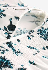 Tissu blanc à imprimé floral bleu, texture froncée, et une ouverture partiellement zippée montrant la doublure intérieure à motif.