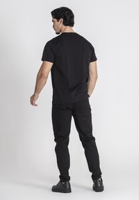 Čierne tričko s krátkym rukávom, jednoduchý dizajn, bavlnený materiál, v kombinácii s čiernymi rifľami a čiernymi topánkami; pohľad zozadu.