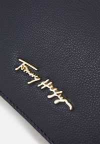 Laumustahautu nahkasilta, jossa on tekstuuri pinta ja kultasävyinen kohokuvioitu logo. Koristeina on ompeleita reunoilla.