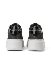 Czarne błyszczące sneakersy z grubymi białymi podeszwami, błyszczącymi zakończeniami pięty oraz brandingiem "KARL LAGERFELD" z tyłu.