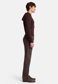 Felpa marrone con cordino regolabile, pantaloni marroni slim-fit e scarpe marroni. Il tessuto appare morbido, con una texture liscia e dettagli minimi.