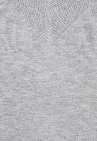 Pull en maille grise avec un design en V, texture lisse et côtes fines le long de l'encolure et des épaules. Apparence minimaliste.