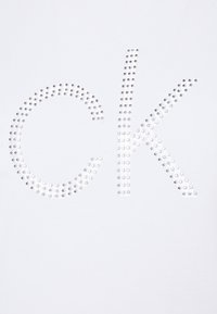 Vit tyg med en stor "CK" design av silver nitar, med en slät textur och ett enkelt, modernt utseende.