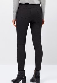 Leggings negros con un patrón de cuadros texturizado, que presentan una silueta ajustada y dos bolsillos traseros, combinados con botas de tobillo.