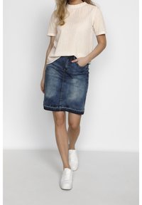 Un haut à manches courtes rayé en pêche clair associé à une jupe en denim bleu délavé arrivant aux genoux et des baskets blanches. La tenue présente un design décontracté.