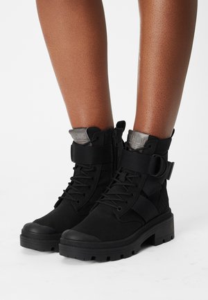 Botas negras de tobillo hechas de ante y material sintético, con cordones, detalles de correa y una suela de goma para mayor tracción.