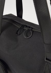 Borsa in tessuto nera con zip superiore e doppi cursori neri. Texture liscia e manici robusti per il trasporto.