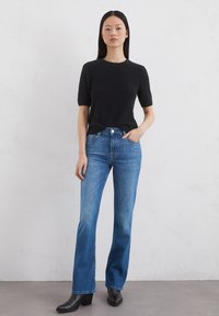Zwart kort mouw gebreid truitje gecombineerd met medium-wash blauwe rechte jeans en zwarte enkellaarsjes met hak.