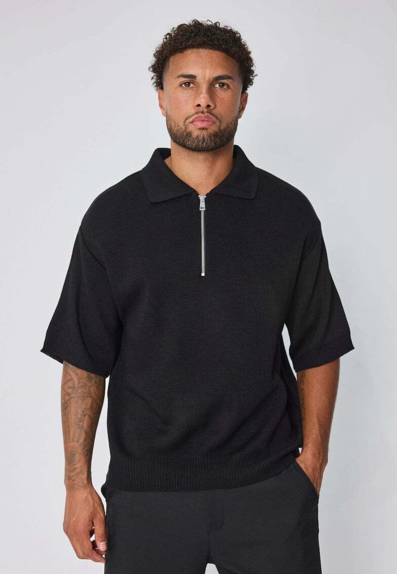 Polo shirt noir à manches courtes avec un col zippé, fabriqué en tissu tricoté texturé, présentant une coupe décontractée et des poignets côtelés.