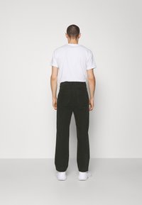 Green corduroy pants with a straight fit, featuring two back pockets, paired with a white t-shirt and white sneakers. Back view.