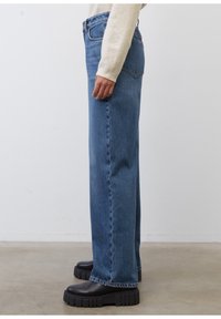 Niebieskie dżinsy prostego kroju z średnim stanem, z klasycznym pięciopocketowym designem. Ubrane z grubosolowymi czarnymi butami na platformie.