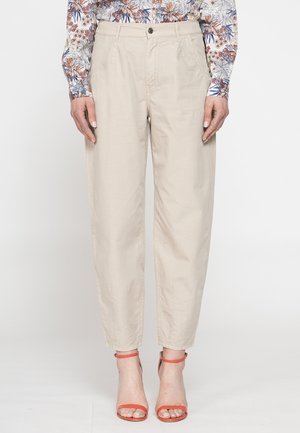 Pantaloni beige casual a vita alta abbinati a sandali arancioni con cinturino alla caviglia e punta aperta e una camicia floreale a maniche lunghe.
