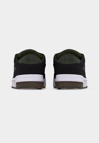 Paire de baskets Vans noires et vert foncé vues de dos, avec des semelles intermédiaires blanches et des semelles extérieures marron sur un fond uni.