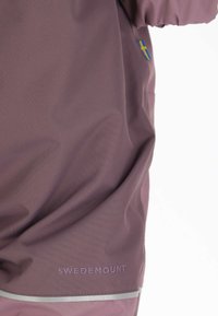 Paarse waterdichte jas gemaakt van glad materiaal, met het "SWEDEMOUNT" logo, reflecterende accenten en een detail van de Zweedse vlag op de mouw.